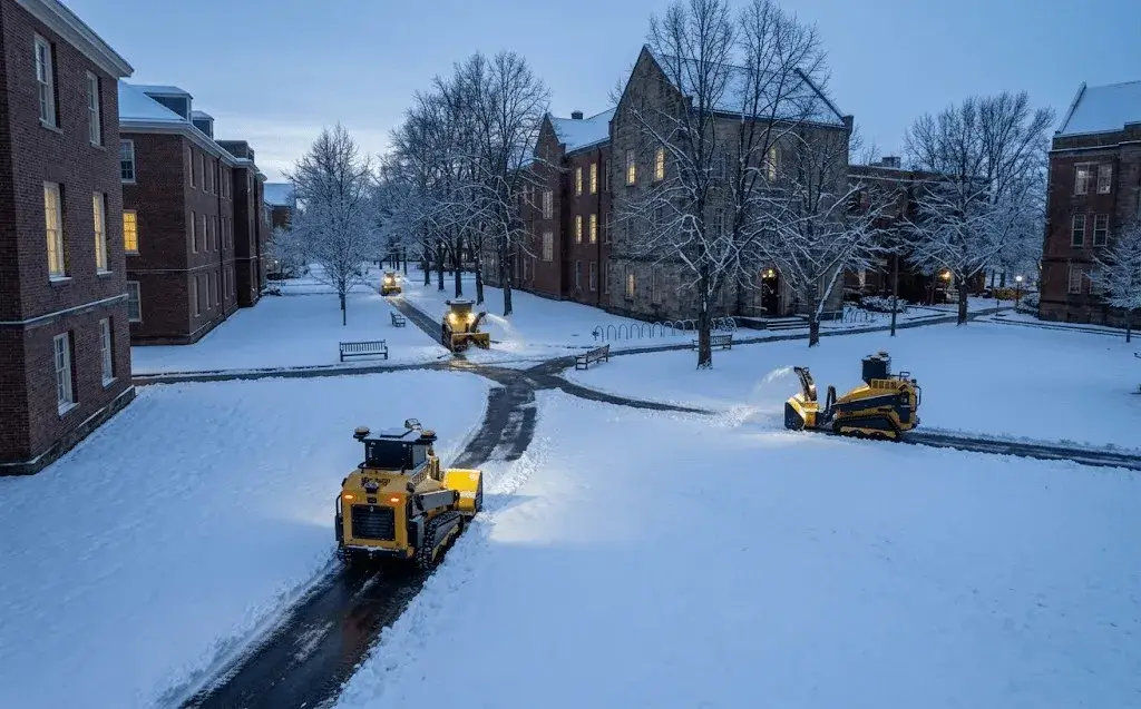 Three SMUR X1 snow robots clearing campus walkways and a service road at first light.